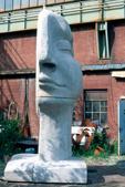Die Skulptur von vorne: halb menschliches Gesicht, halb Scheibe